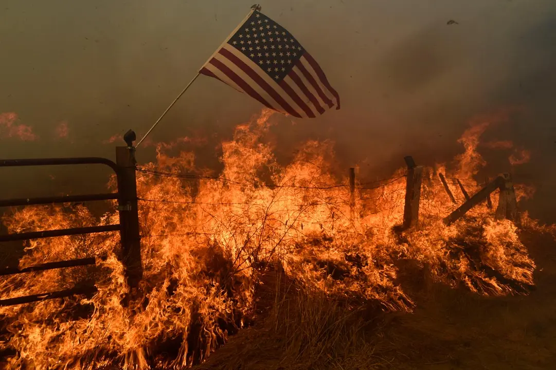 A US flag flies above a fire on an area in southern Santa Clara County during the spread of forest fires. Photo: Neal Waters/ZUMA Wire/dpa
