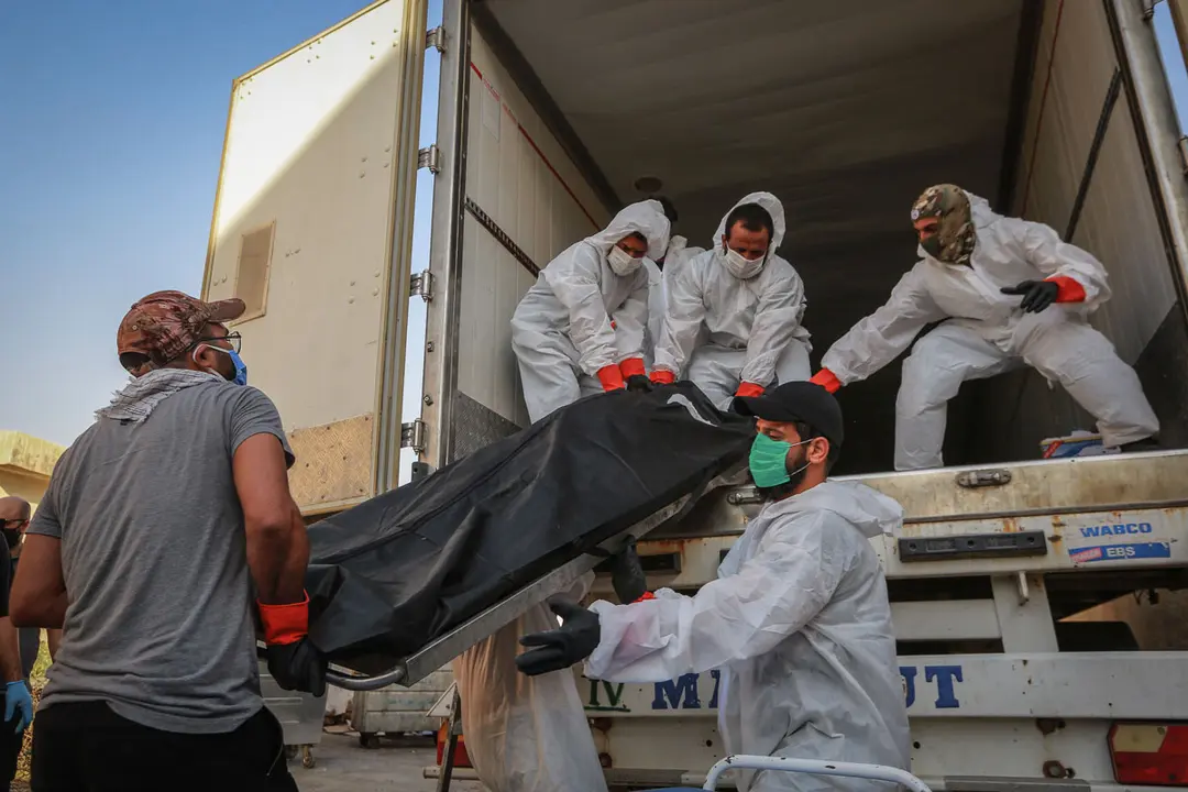 Iraq: Workers wearing full protective gear load bodies of people who died due to the coronavirus, into a refrigerator truck of the Popular Mobilization Forces (PMF) to be transferred from Baghdad to Wadi Al-Salam Cemetery in the city of Najaf. Photo: Ameer Al Mohammedaw/dpa