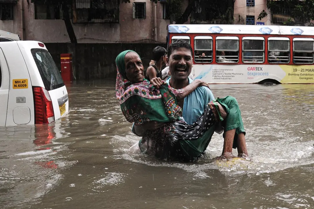 India, Mumbai: A man carries an elderly woman as he wades through the flood waters caused by monsoon rains. Photo: Ashish Vaishnav/dpa.