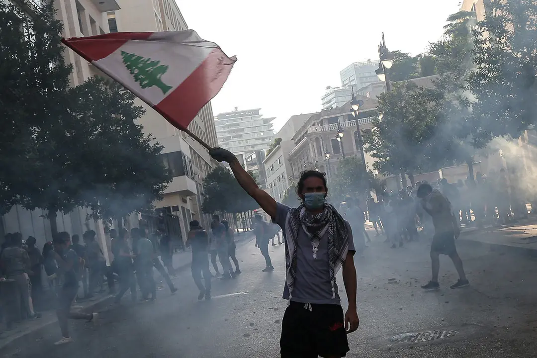 10 August 2020, Lebanon, Beirut: An anti-government activist flies the Lebanese national flag during clashes with riot police in Beirut&#39;s downtown. The Lebanese government resigned following the massive Beirut port explosion of 04 August which killed at least 158 people, wounded 6000 and displaced some 250,000 to 300,000. Photo: Marwan Naamani/dpa.