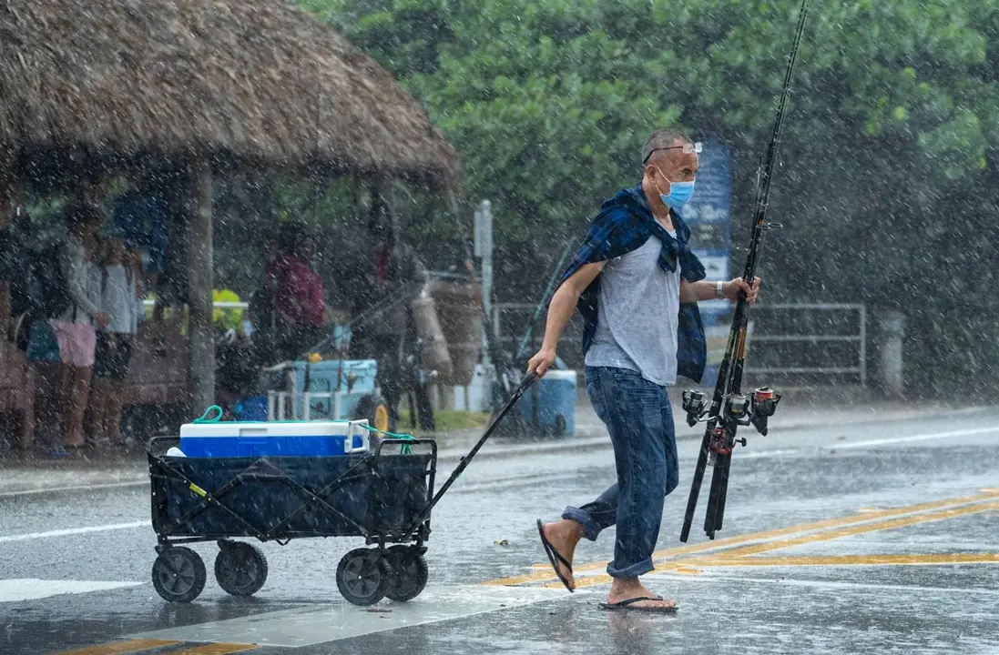 19 August 2020, US, Juno Beach: A fisherman hurries across a street during a heavy rain at the Juno Beach Pier. Photo: Greg Lovett/dpa.