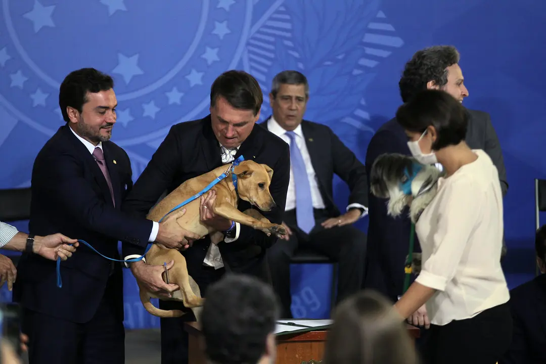 29 September 2020, Brazil, Brasilia: Brazilian President Jair Bolsonaro (C) carries his dog as he signs the Bill that alters and aggravates penalties for mistreatment of animals. Photo: Jorge William/dpa.