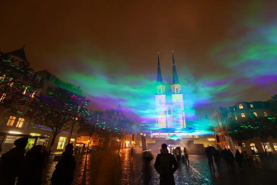 15 October 2020, Saxony-Anhalt, Halle (Saale): Passers-by look at artificially generated auroras on the Hallmarkt using laser beams and fog. Photo: Jan Woitas/dpa.