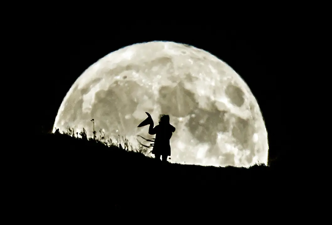 31 October 2020, England, Leeds: A person holding a witch&#39;s hat watches the Blue Moon rising over Castle Hill in Huddersfield. Photo: Danny Lawson/dpa.