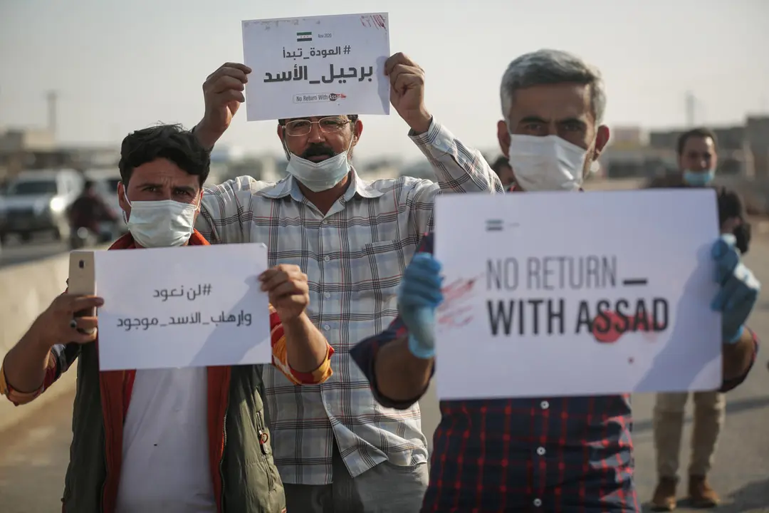 12 November 2020, Syria, Sarmada: Internally displaced persons and employees of civil society organizations hold placards demanding Syrian President Bashar al-Assad to step down so that they can return, during a protest against the international conference on the return of refugees that was held in Damascus. Photo: Anas Alkharboutli/dpa.