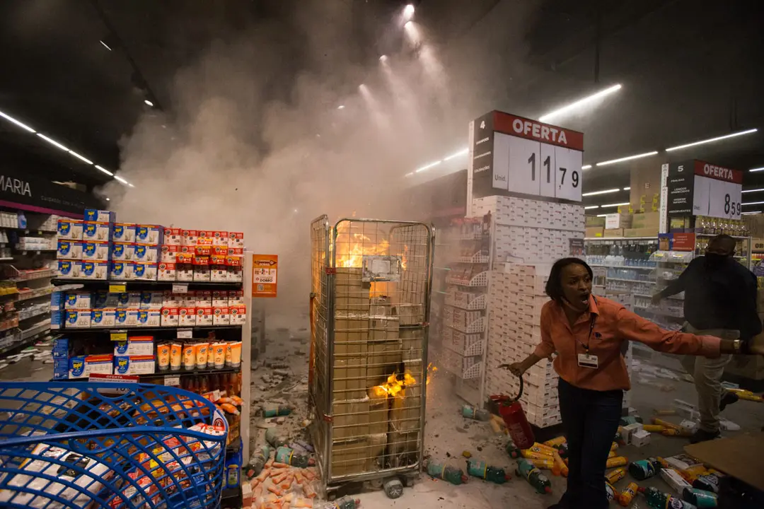 20 November 2020, Brazil, Sao Paulo: An employee tries to put out a fire started by demonstrators in a Carrefour supermarket during a protest on Black Awareness Day against racism and the death of a man who was brutally beaten by two security men in front of a supermarket. Photo: Andre Lucas/dpa.