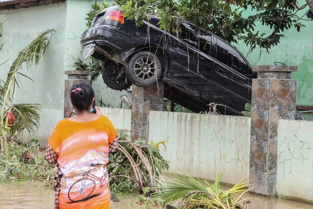 04 December 2020, Indonesia, Medan: A woman walks near the wreck of a car that was washed away by the floods after the nearby river overflow. Photo: Albert Ivan Damanik/ZUMA Wire/dpa