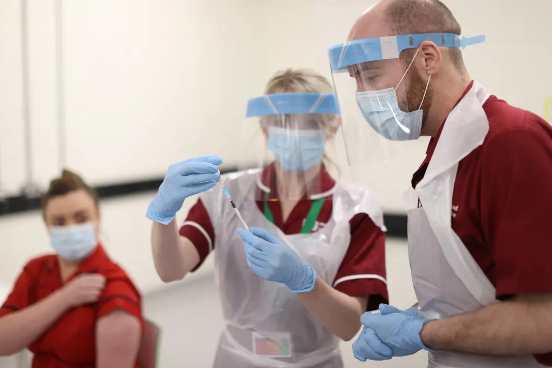 08 December 2020, Northern Ireland, Belfast: Nurse practitioners fill a needle with the Covid-19 vaccine before injecting Sister Joanna Sloan (L), the first person in Northern Ireland to receive the first of two Pfizer/BioNTech Covid-19 vaccine jabs, at the Royal Victoria Hospital on the first day of the largest immunisation programme in the UK's history. Photo: Liam Mcburney/PA Wire/dpa