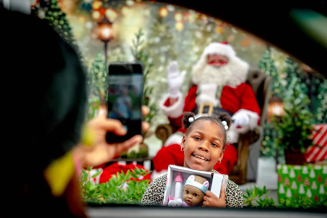 11 December 2020, US, San Bernardino: A girl holds a doll she received as she poses for a picture with Santa Clause during a drive-thru toy giveaway at Valley College. Photo: Watchara Phomicinda/dpa.