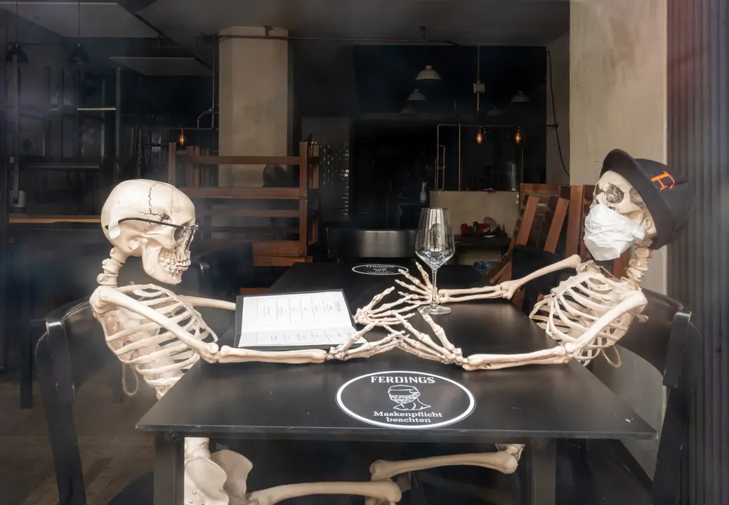 18 January 2021, Bavaria, Munich: Two skeletons installed on a table are seen from the window of a closed restaurant in downtown. Photo: Peter Kneffel/dpa