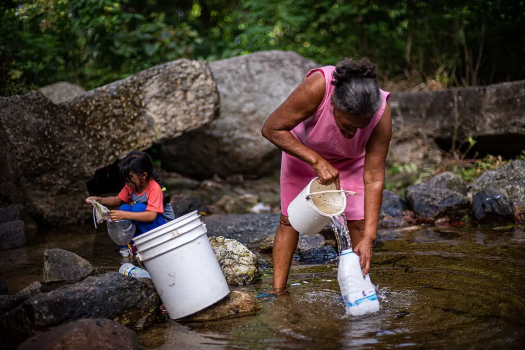 27 January 2021, Venezuela, Valencia: An elderly woman fills a water container from a river, as the country has a severe water shortage. Photo: Elena Fernandez/ZUMA Wire/dpa