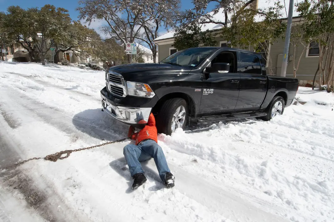 15 February 2021, US, Austin: A motorist tries to hook a chain to his truck stuck for several hours in downtown Austin after a rare snowstorm overnight in central Texas. Austin is shut down waiting for a temperature rise later this week. Photo: Bob Daemmrich/ZUMA Wire/dpa