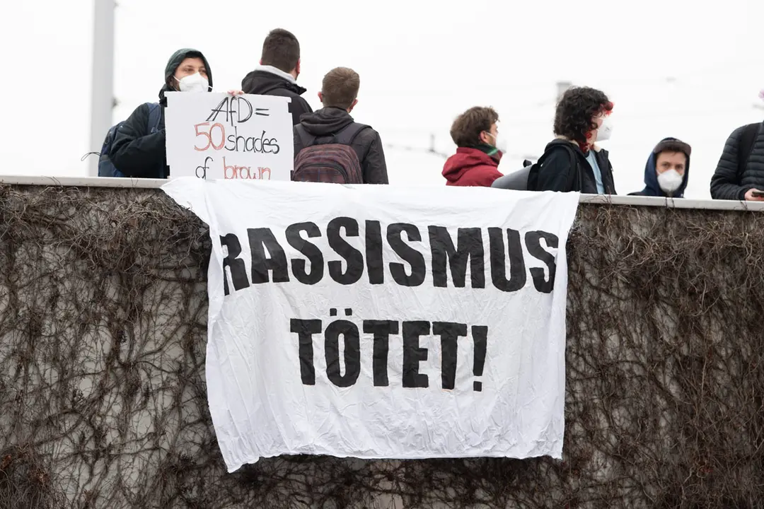 10 April 2021, Saxony, Dresden: Demonstrators stand with banners with the inscription "Racism kills!" at an access road to the exhibition grounds during the Alternative for Germany (AfD) party conference. Photo: Sebastian Kahnert/dpa-Zentralbild/dpa