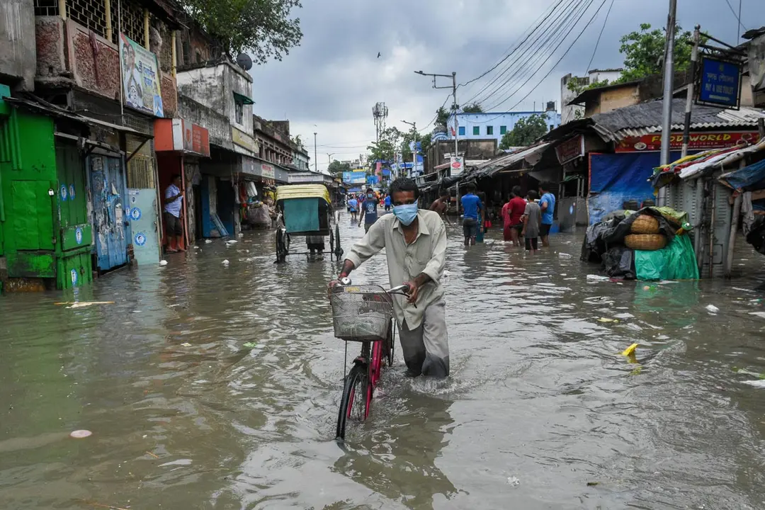 26 May 2021, India, Kolkata: A man pushes his bicycle as he wades through the water at a flooded road in the wake of cyclone "Yaas". A powerful storm hit India's east coast on Wednesday, flattening houses, uprooting trees and electric poles, breaking down sea embankments and flooding large tracts of land. Photo: Debarchan Chatterjee/ZUMA Wire/dpa