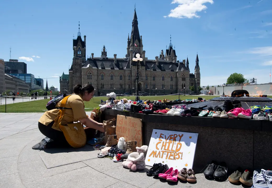 31 May 2021, Canada, Ottawa: An indigenous kneels in front of shoes placed on the Centennial Flame to honour more than 200 children whose remains have been found buried at a former residential school in Kamloops. Photo: Adrian Wyld/The Canadian Press via ZUMA/dpa