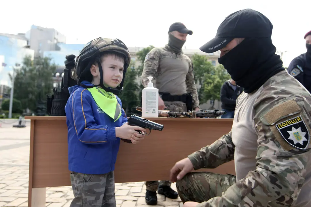01 June 2021, Ukraine, Kiev: A masked police officer kneels by a little boy holding a firearm during the celebration of International Children’s Day in Sofiiska Square. Photo: -/Ukrinform/dpa