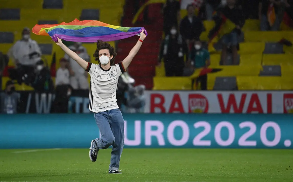 23 June 2021, Bavaria, Munich: A young man runs across the pitch with a rainbow flag prior to the start of the UEFA EURO 2020 Group F soccer match between Germany and Hungary at the Allianz Arena. Photo: Federico Gambarini/dpa.