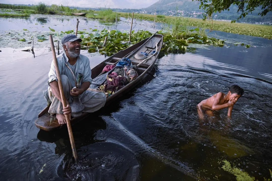 05 July 2021, India, Srinagar: A boy bathes next to a man who sits in his boat in the water of Dal Lake during a sunny day in Srinagar. Photo: Idrees Abbas/SOPA Images via ZUMA Wire/dpa.