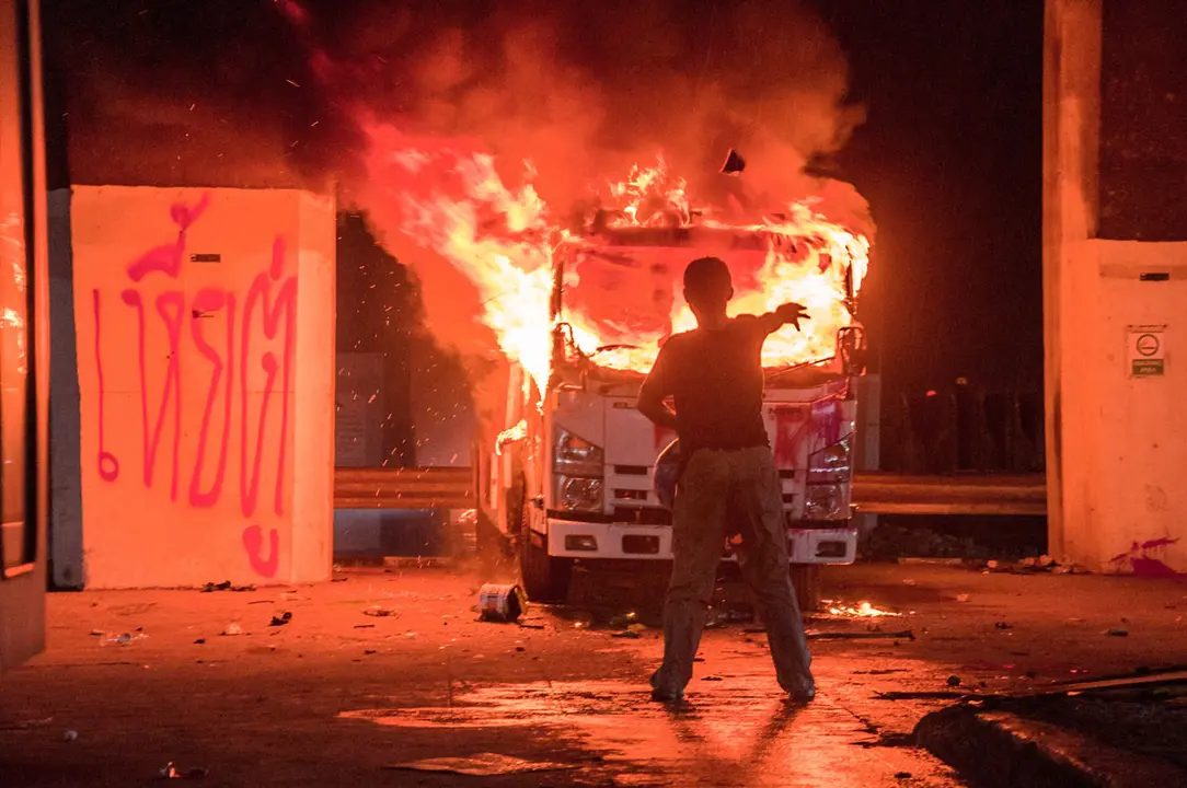 11 August 2021, Thailand, Bangkok: A demonstrator stands in front of a burning truck during an anti-government protest to demand the resignation of Prime Minister Prayut Chan-o-cha and the redistribution of part of the budget for the monarchy and the military for the fight against the coronavirus. Photo: Peerapon Boonyakiat/SOPA Images via ZUMA Press Wire/dpa