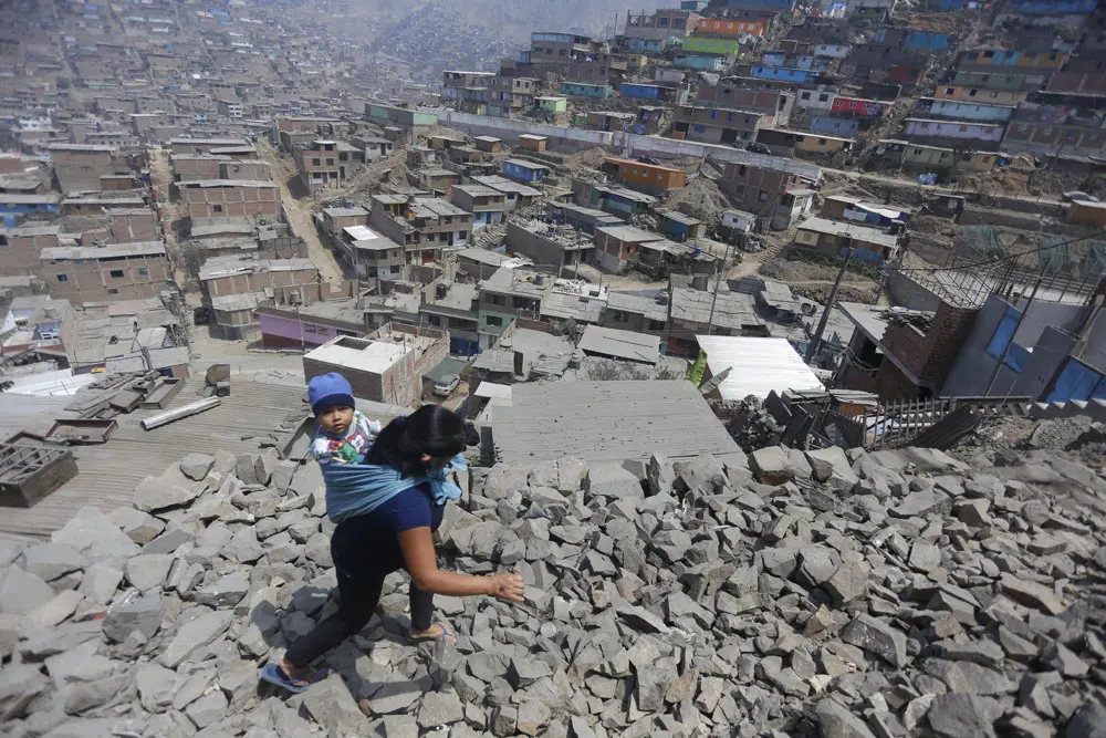 10 September 2021, Peru, Lima: A woman carries her child on her back and walks over rocks to a house where food is being distributed in the midst of the Corona pandemic. Photo: Gian Masko/dpa.