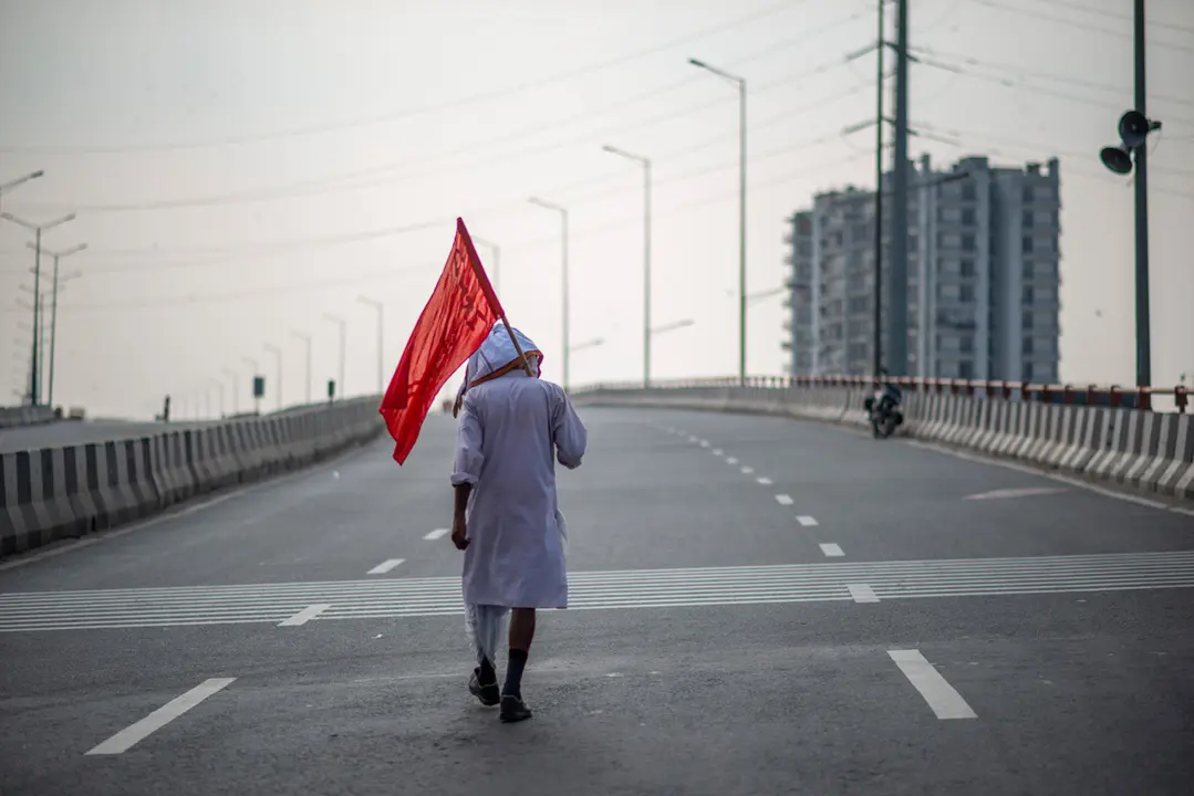 27 September 2021, India, Ghaziabad: A farmer with a flag walks on a deserted Road during farmers nationalwide strike against the central government's three farm reform laws. Photo: Pradeep Gaur/SOPA Images via ZUMA Press Wire/dpa