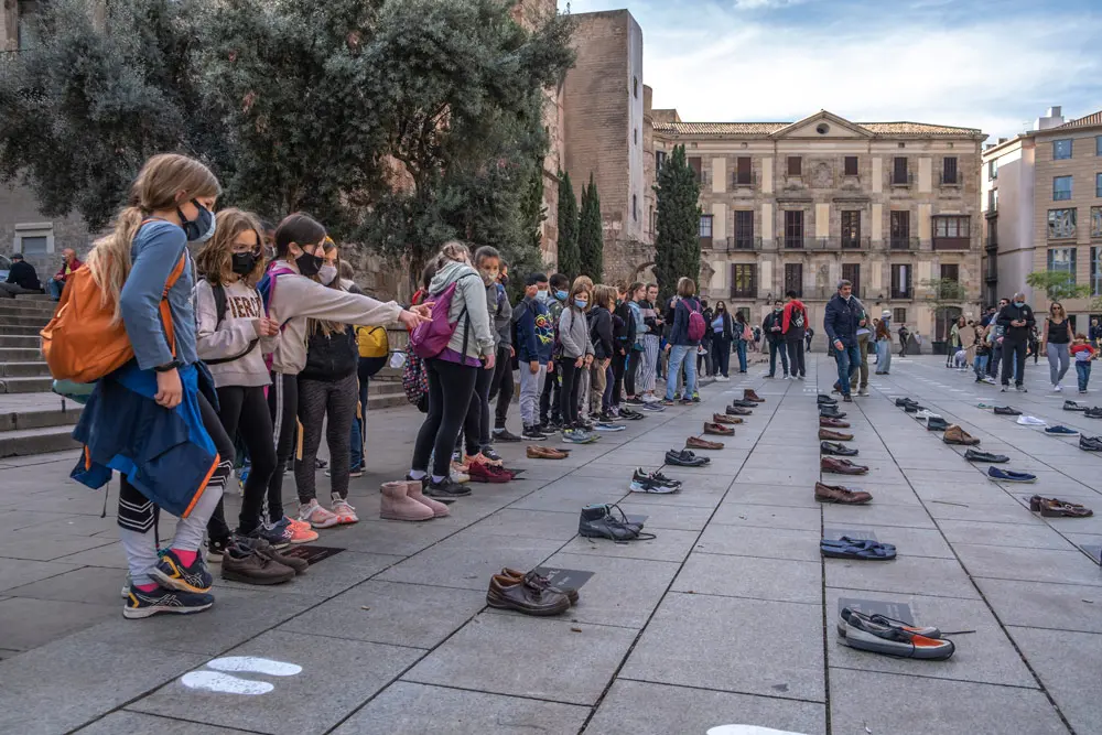 27 October 2021, Spain, Barcelona: Primary school students look at the memorial project entitled "Petjadas contra l, oblit" (Footprints against oblivion) at the Cathedral of Barcelona plaza in memory of the homeless who died in 2021 and those who live on the streets. The project displays 68 pairs of shoes and 1064 footprints. Photo: Paco Freire/SOPA Images via ZUMA Press Wire/dpa.