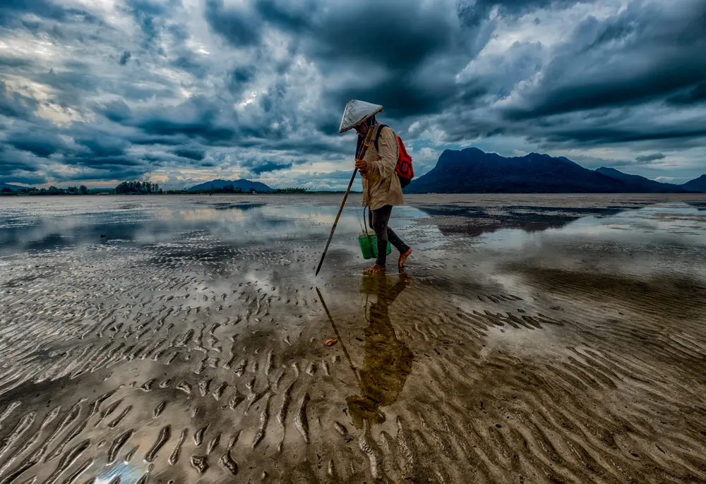 13 November 2021, Malaysia, Kuching: Noriah Nor, 62, looks for bamboo snails (ambal) on the beach of Kampung Buntal, a fishing village located about 30 kilometres from Kuching city. When the seawater recedes at low tide the inhabitants use the seabed as a food source. Photo: Rushdan Manan/BERNAMA/dpa