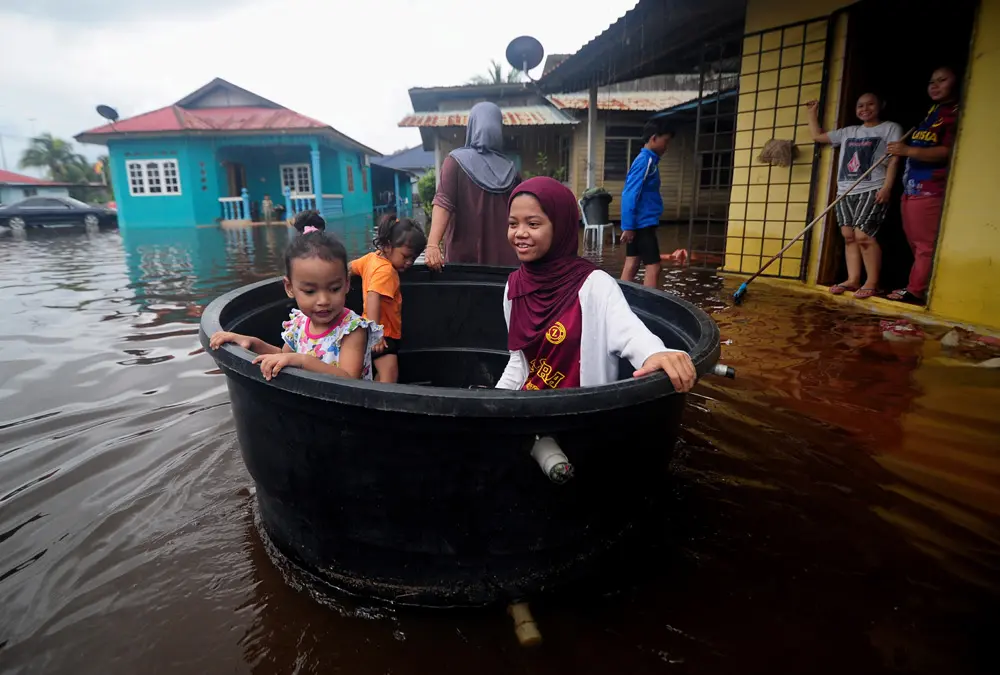 19 December 2021, Malaysia, Shah Alam: A woman uses a water tank to carry her children after a residential area was hit by floods due to continuous heavy rain that hit several places in Malaysia yesterday. Photo: Mohd Asri Saifuddin Mamat/BERNAMA/dpa.