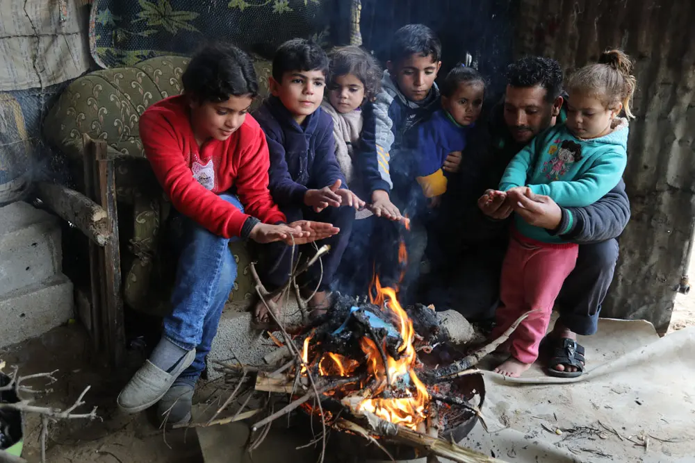 23 December 2021, Palestinian Territories, Beit Lahia: A Palestinian family warm themselves by a fire at their home on a cold rainy day in Beit Lahia. Photo: Ashraf Amra/APA Images via ZUMA Press Wire/dpa