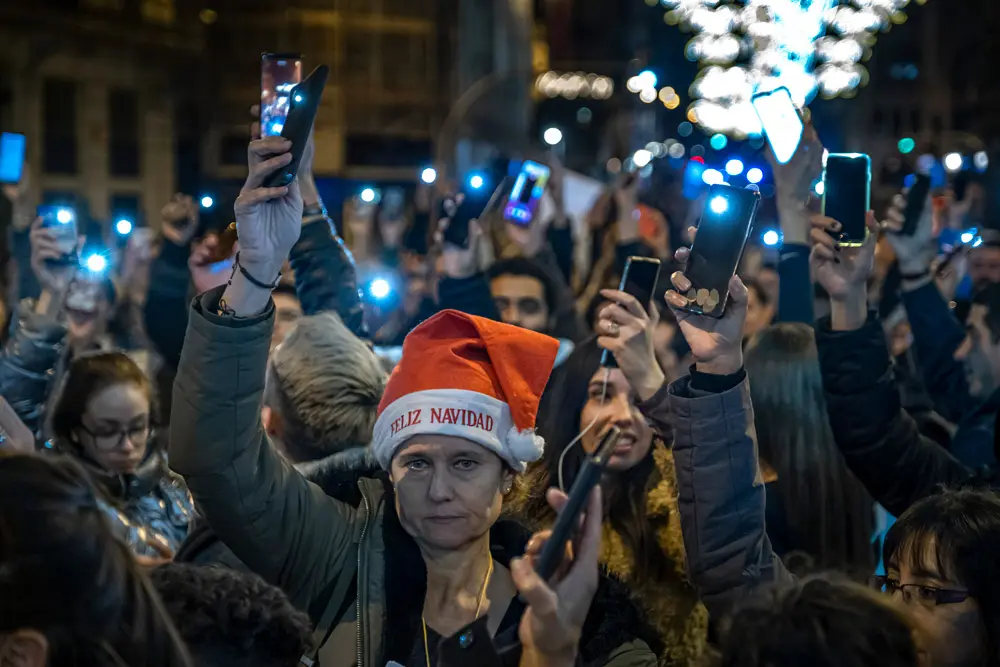 25 December 2021, Spain, Barcelona: A protester wearing a Santa hat raises her lighting mobile phone during a protest against the vaccination and the Covid passport in the centre of Barcelona on Christmas day. Photo: Paco Freire/SOPA Images via ZUMA Press Wire/dpa.
