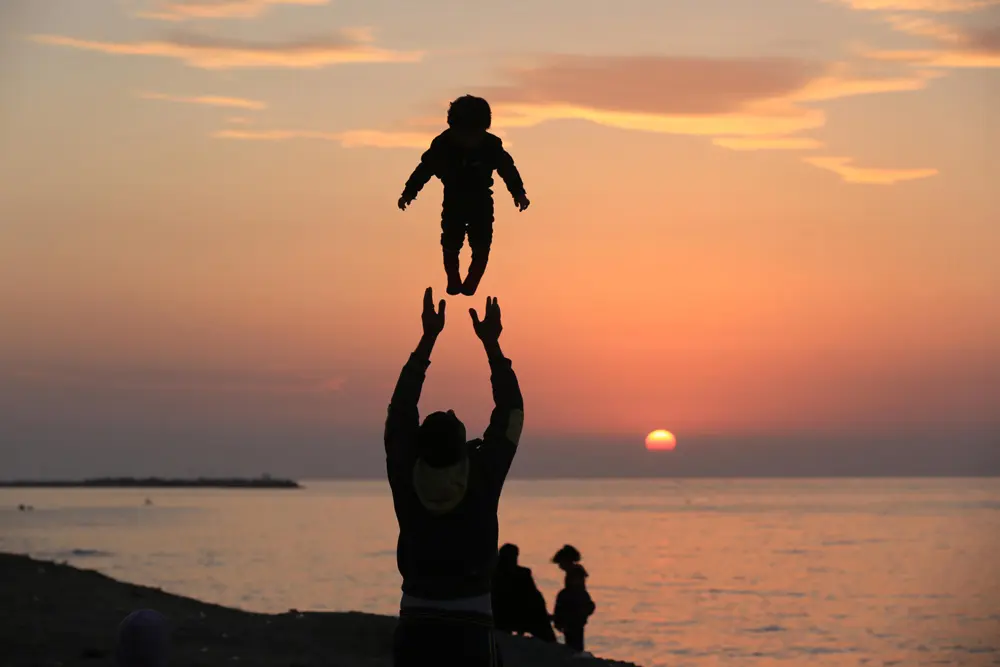 28 December 2021, Palestinian Territories, Gaza: A Palestinian man throws up a little son on the beach of Gaza sea during sunset. Photo: Ashraf Amra/APA Images via ZUMA Press Wire/dpa.