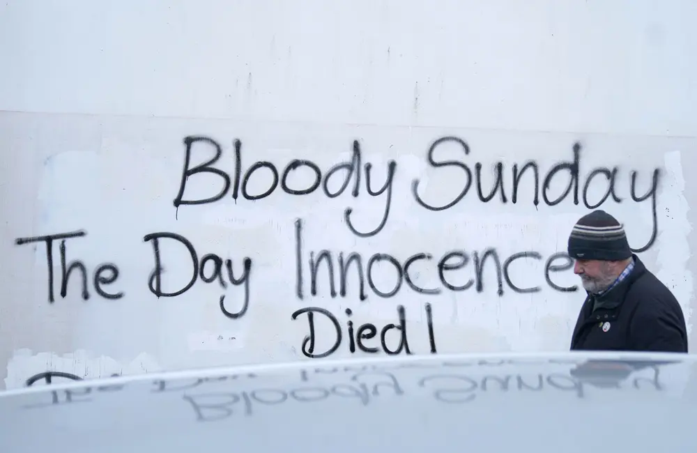 30 January 2022, Northern Ireland, Londonderry: A man walks past graffiti on a wall in the Creggan area of Derry ahead of a remembrance walk to mark the 50th anniversary of Bloody Sunday, where British soldiers shot 28 unarmed civilians during a protest march against internment in Londonderry in 1972. Photo: Brian Lawless/PA Wire/dpa.