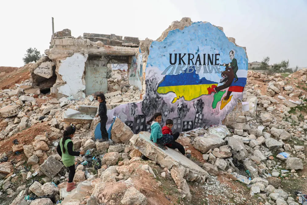 24 February 2022, Syria, Binnish: Syrian children sit next to a mural painted by painters in solidarity with Ukraine on a wall of a destroyed home in the wake of the Russian invasion of Ukraine. Photo: Anas Alkharboutli/dpa.