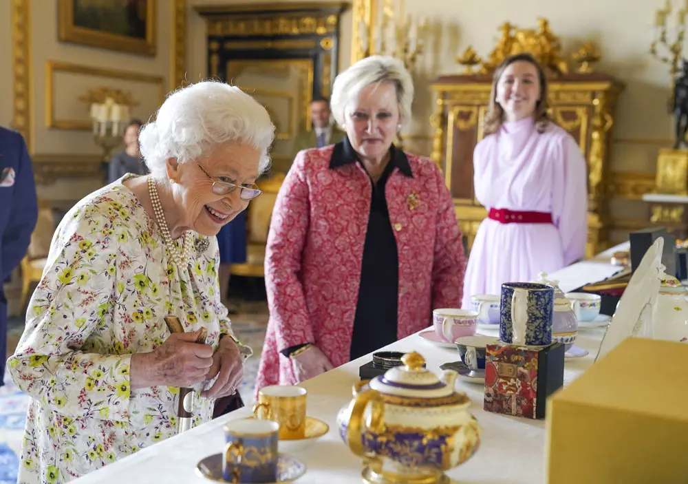23 March 2022, United Kingdom, Windsor: Queen Elizabeth II (L) talks to Pamela Harper (C) from British craftwork company, Halcyon Days, as she views a display of artefacts to commemorate the company's 70th anniversary in the White Drawing Room at Windsor Castle, Berkshire. Photo: Steve Parsons/PA Wire/dpa.