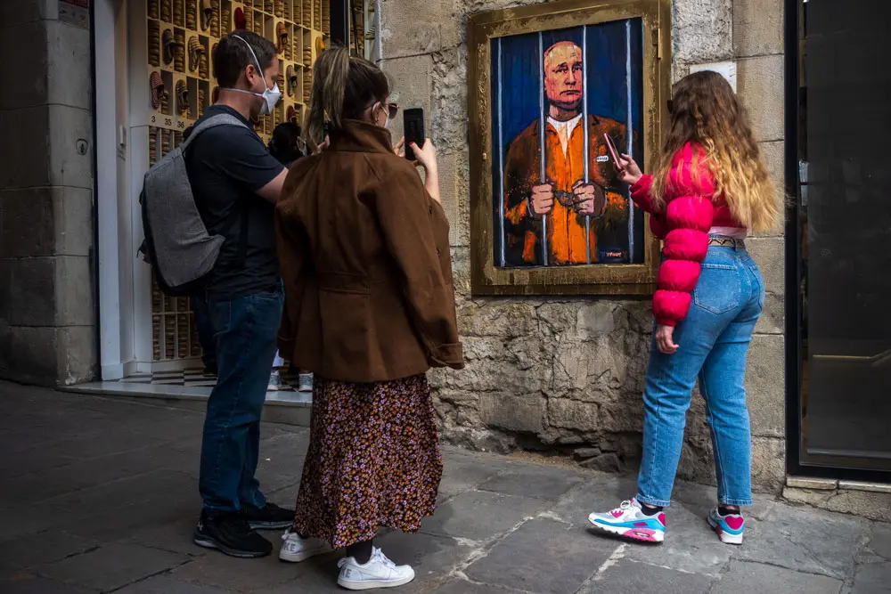 28 March 2022, Spain, Barcelona: Passers-by take a photo of a graffiti by Italian urban artist 'TVBoy', Salvatore Benintende, titled 'The Dream' depicting Russian president Vladimir Putin imprisoned behind bars, in protest to the ongoing Russian attacks on Ukraine. Photo: Matthias Oesterle/ZUMA Press Wire/dpa.