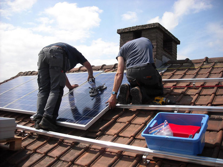 Workers placing solar panels to produce energy on a roof. Photo: Pixabay.
