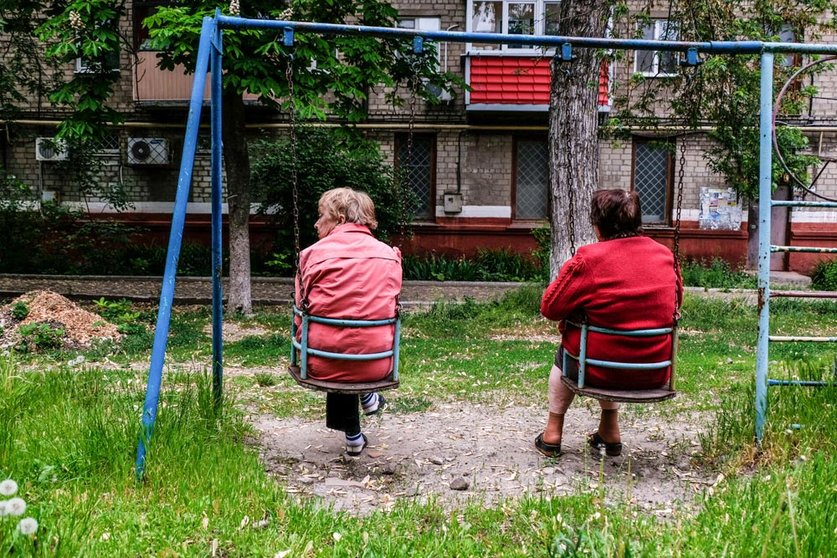 21 May 2022, Ukraine, Kramatorsk: Elderly women sit on swings in a playground in front of their damaged houses in Kramatorsk. Kramatorsk is a city in the Donetsk region known for its metallurgical industry, particularly the production of iron and steel. Photo: Rick Mave/SOPA Images via ZUMA Press Wire/dpa.