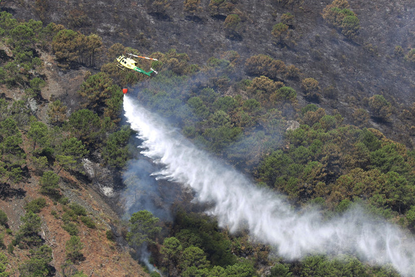 10 June 2022, Spain, Pujerra: A firefighting helicopter pours water over a burned area to control a wild fire near Pujerra on the Costa del Sol. Photo: Álex Zea/EUROPA PRESS/dpa.
