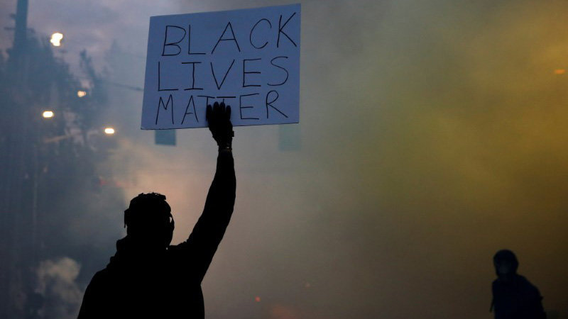 A person holds a &#34;Black Lives Matter&#34; sign as a heavy cloud of tear gas and smoke rises after being deployed by Seattle police as protesters rally against police brutality and the death in Minneapolis police custody of George Floyd, in Seattle, Washington, U.S. June 1, 2020. Picture taken June 1, 2020. REUTERS/Lindsey Wasson