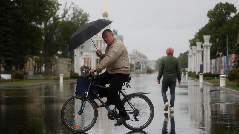 A man holding an umbrella rides a bicycle at the Exhibition of Achievements of National Economy (VDNKh) on the first day of reopening following the easing of lockdown measures, which were introduced amid the outbreak of the coronavirus disease (COVID-19) in Moscow, Russia June 1, 2020. REUTERS/Maxim Shemetov