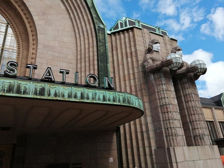 A view of Helsinki&#39;s central station, with the stone men who guard the entrace equipped with face masks. Photo: Foreigner.fi.