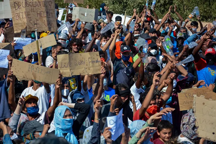 11 September 2020, Greece, Lesbos: Immigrants and refugees hold placards during a protest near the burnt-out refugee camp Moria, that was almost completely destroyed in a fire the broke out on Wednesday. More than 12,000 migrants, who lost what homes they had in the blaze that might have been intentionally set, had to spend the night on the streets. Photo: -/Eurokinissi/dpa.