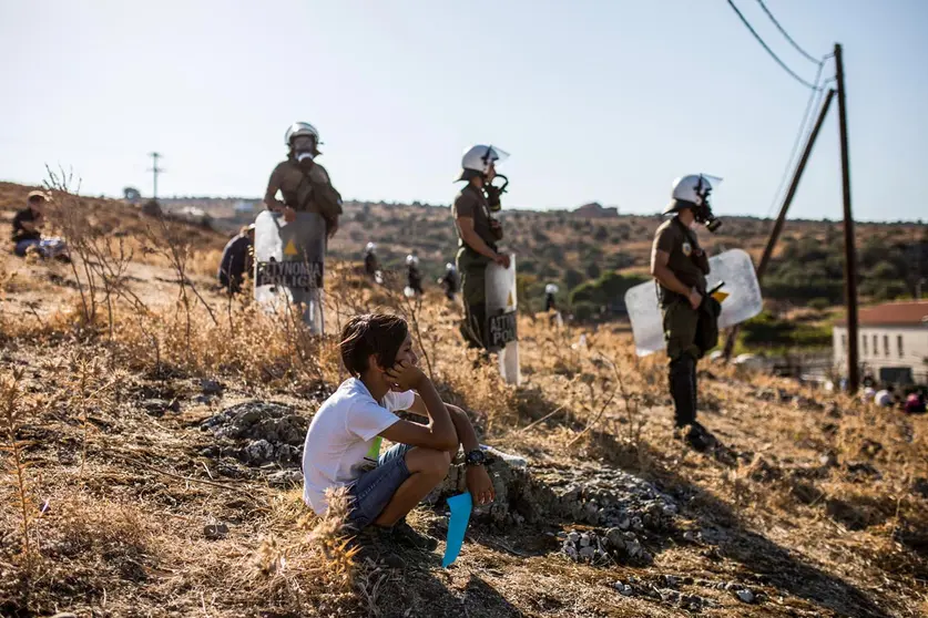 11 September 2020, Greece, Moria: A boy sits in front of policemen as migrants take part in a protest to call for their resettlement after the massive fire that burnt out the refugee camp of Moria which almost destroyed it, leaving more than 12,000 migrants homeless. Photo: Socrates Baltagiannis/dpa