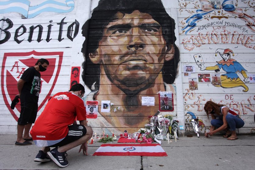 25 November 2020, Argentina, Buenos Aires: People place flowers and candles in front of a mural depicting the Argentinian legend Diego Mardona outside the Argentinos Juniors football club, where Maradona started his career. Argentina football great Diego Maradona has died at the age of 60, the Argentinian Football Association said on Wednesday. Photo: Carol Smiljan/ZUMA Wire/dpa.
