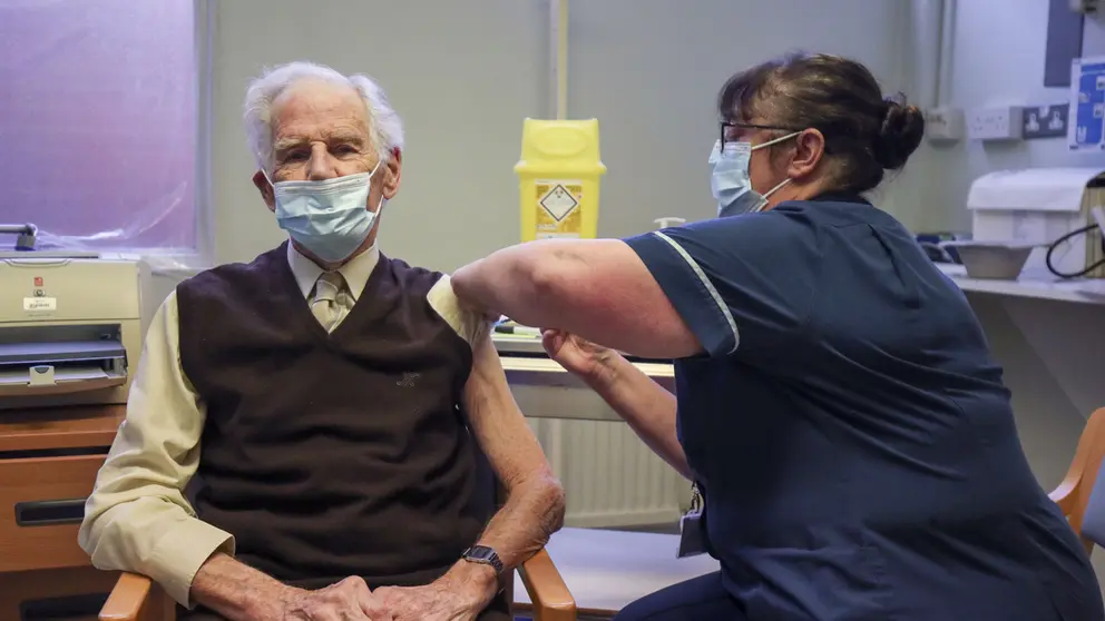 14 December 2020, England, Chalfont Saint Peter: Brian Horne receives the first of two injections with a dose of the Pfizer/BioNtech covid-19 vaccine from Nurse Helen Ellis at a GP led clinic, as hundreds of Covid-19 vaccination centres run by local doctors begin opening across England. Photo: Steve Parsons/PA Wire/dpa.