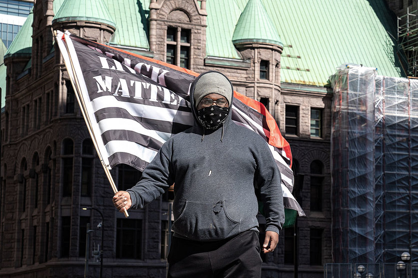 12 March 2021, US, Minneapolis: A man waves the flag of black live matters while standing outside the Hennepin County Courthouse during the trial of former Minneapolis Police officer Derek Chauvin who's involved in the death of George Floyd on 25 May 2020. The family of Floyd has reached a 27 US million dollars settlement with the city of Minneapolis in a civil lawsuit over his death. Photo: Glen Stubbe/TNS via ZUMA Wire/dpa