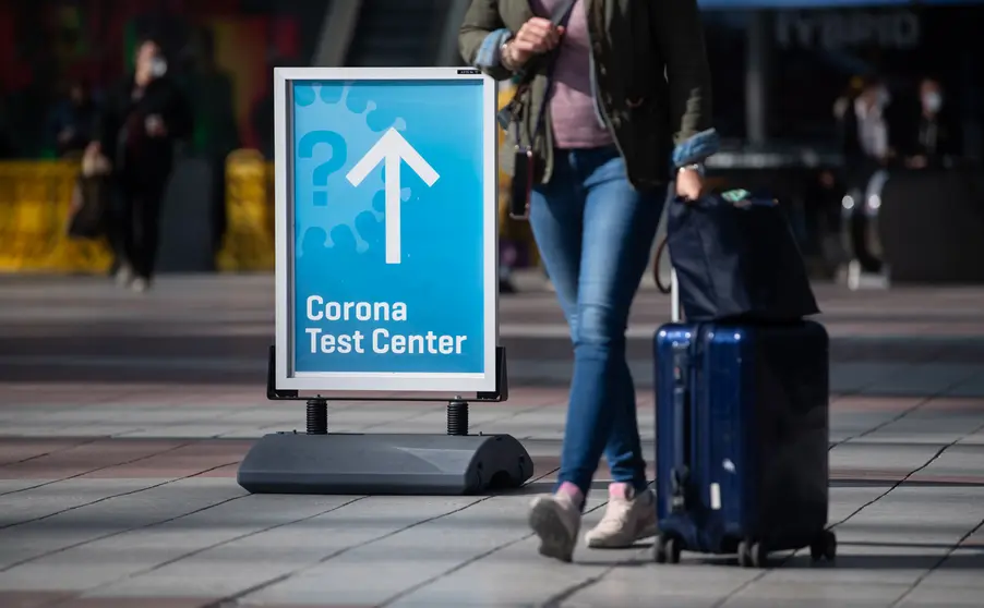 26 March 2021, Bavaria, Munich: A woman passes past a sign with the inscription "Corona Test Center" at Munich airport. A new requirement for people arriving at German airports to have submitted to coronavirus testing has been postponed from Sunday to Tuesday. Photo: Sven Hoppe/dpa