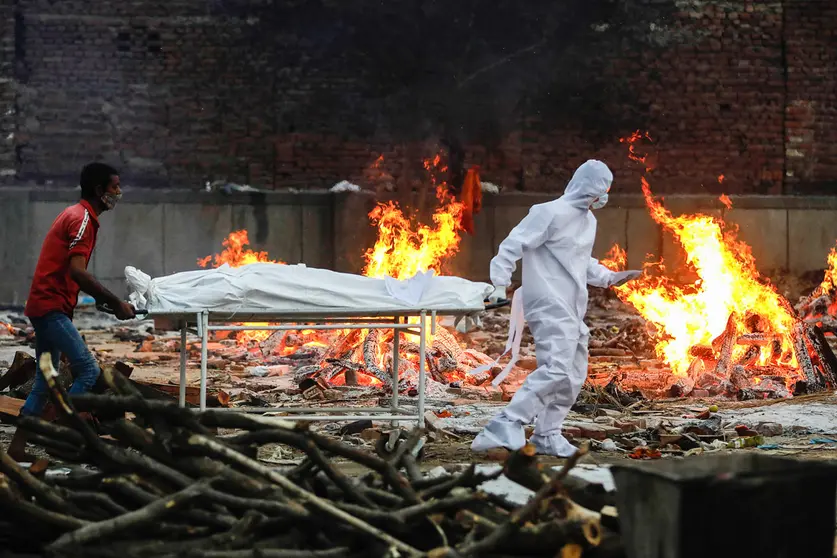 09 May 2021, India, New Delhi: A relative and a health worker carry a body of Coronavirus (Covid-19) victim during a cremation at a crematorium in New Delhi. Photo: Amarjeet Kumar Singh/SOPA Images via ZUMA Wire/dpa