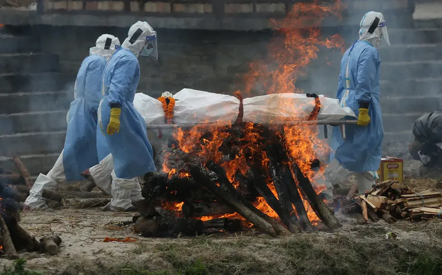 04 May 2021, Nepal, Kathmandu: Men wearing personal protective suits carry the body of a COVID-19 victim for cremation on the bank of Bagmati River. Photo: Dipen Shrestha/Zuma Press/dpa