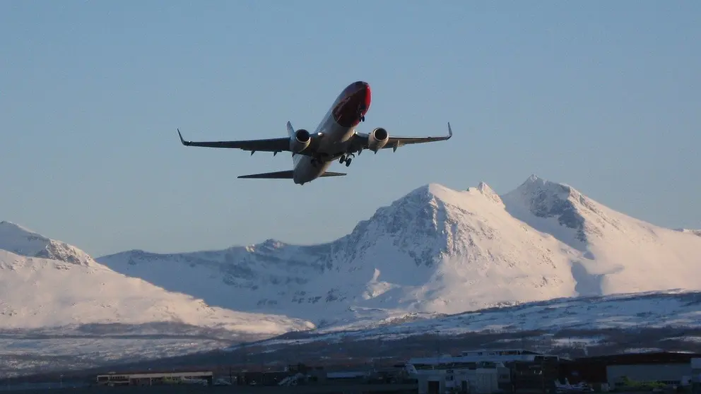 A Norwegian plane flies over a lake and snowy hills. Photo: Petteri Jokela/Pixabay.